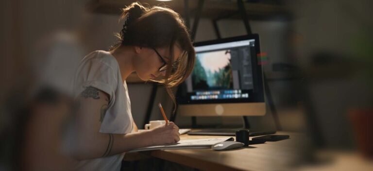 mujer joven realizando un boceto de diseño gráfico en su escritorio frente al ordenador